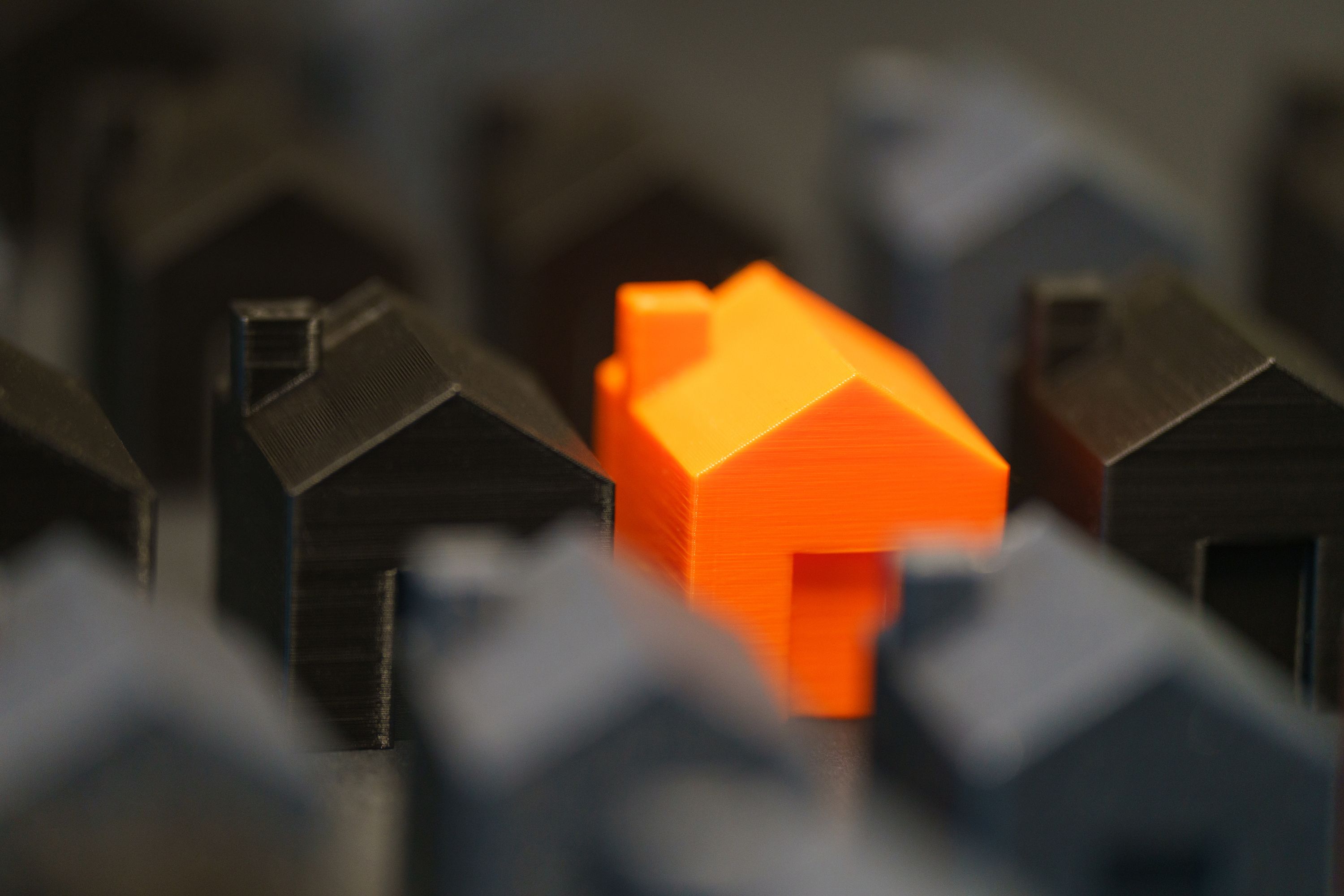 vibrant orange model house stands out among black miniature houses, symbolizing real estate concepts